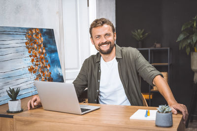 Portrait of young man using laptop at office