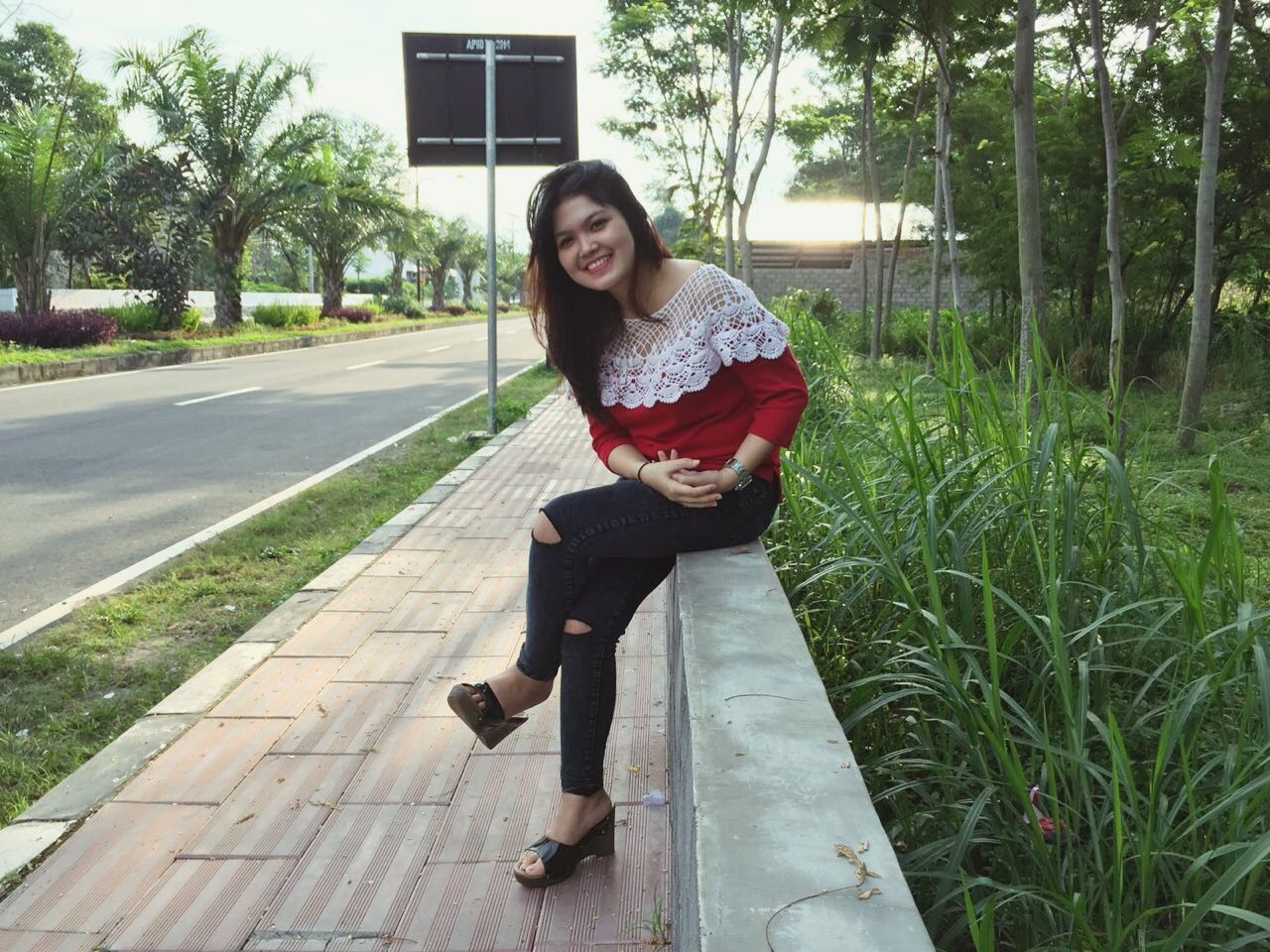 one person, full length, real people, tree, front view, young adult, looking at camera, lifestyles, sitting, young women, outdoors, leisure activity, happiness, day, smiling, portrait, grass, building exterior, beautiful woman, nature, architecture