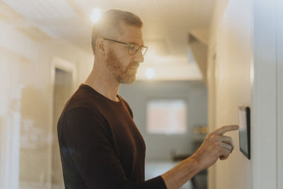 Mature man adjusting room lights through digital tablet mounted on wall at modern home