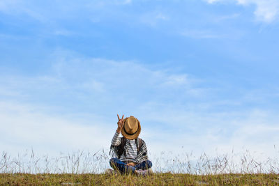 Girl sitting on grassy field against blue sky