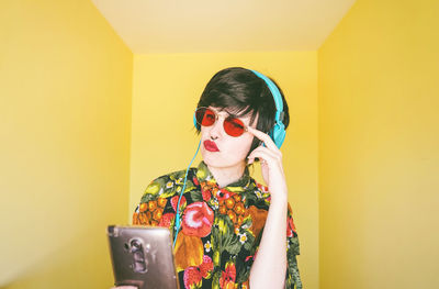Woman wearing sunglasses using phone against colored background