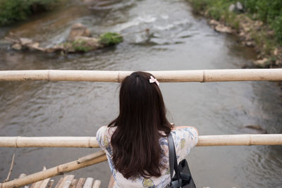 Rear view of woman standing on footbridge over river