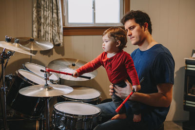 Father holding cute baby son playing drums at home