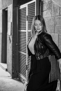 Young woman standing on footpath against wall