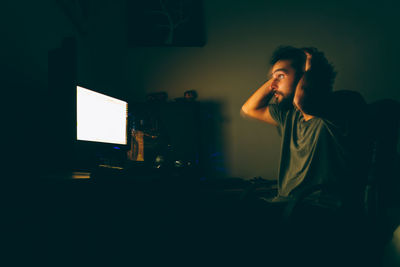 Blurred motion of man looking at illuminated computer in darkroom