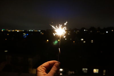 Cropped hand holding sparkler against sky at night