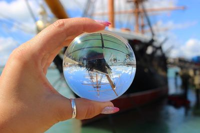 Close-up of hand holding crystal ball against sky