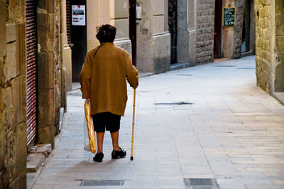 Rear view of senior woman walking on footpath amidst buildings in city