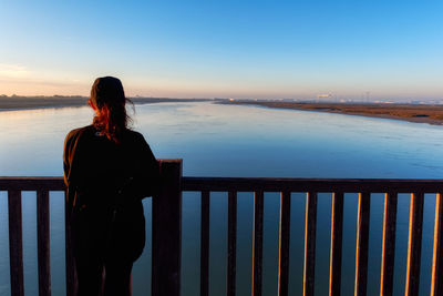 Rear view of woman looking at river against sky during sunset