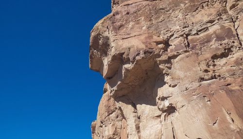 Low angle view of rock formation suggesting human characteristics against clear blue sky