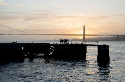 Silhouette bridge over sea against sky during sunset