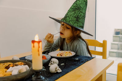 Girl child in a witch hat eats halloween food.