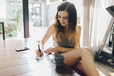 Smiling young woman writing at home