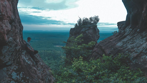 Man wearing cap standing on rock formation against sky