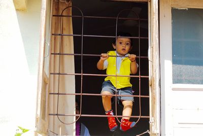 Portrait of cute boy climbing on window with mother standing in background