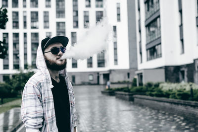 Young man smoking while standing against building