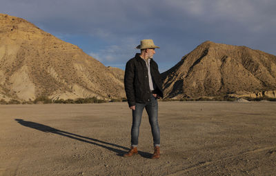 Adult man in cowboy hat standing against mountains in tabernas desert. almeria, spain