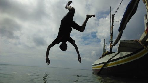 Low angle view of man jumping in sea against sky