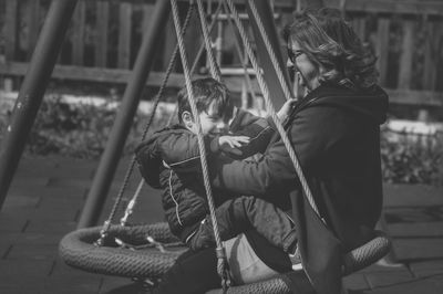 Side view of grandmother with grandson sitting on swing at playground