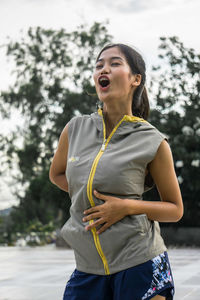 Young woman laughing while standing against trees