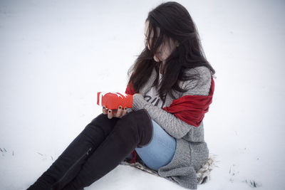High angle view of woman holding gift while sitting on snow