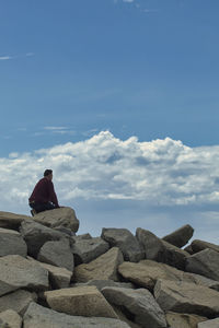 Man on top of a stone breakwater looking at the horizon with clouds in the background