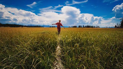 Young man walking on grassy field against cloudy sky during sunny day