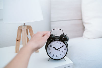 Woman touching alarm clock at 7 am on bedroom during morning, wake up concept
