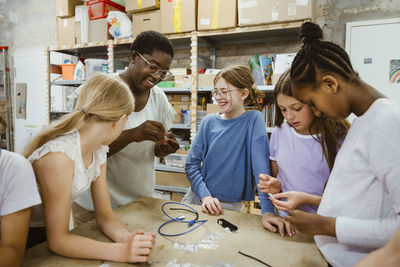 Female students with teacher holding electric component near table in workshop at school