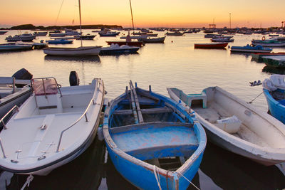 Boats moored in harbor at sunset