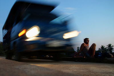 Blurred motion of vehicle moving on road by man during sunset