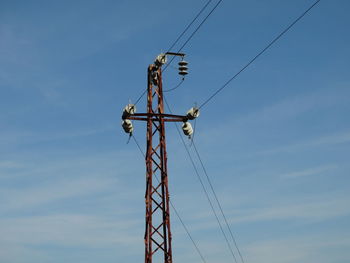 Low angle view of electricity pylon against blue sky