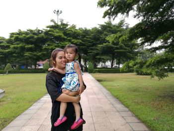 Happy mother carrying daughter while standing on footpath at public park