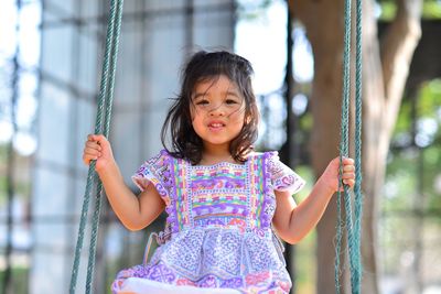 Portrait of cute girl sitting on swing at playground