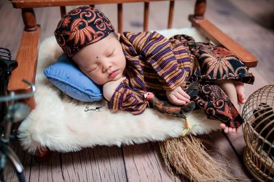 High angle view of baby boy in traditional clothing on small sofa