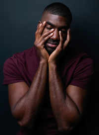 Man with hands on face against black background