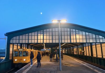 People walking on illuminated railroad station against clear sky