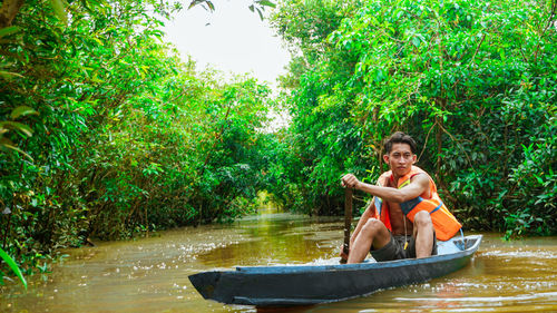 Portrait of man sitting on riverbank against trees