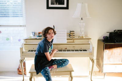 Teen girl sitting on piano bench touches the piano keys behind her