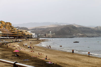 People at beach by mountains against clear sky