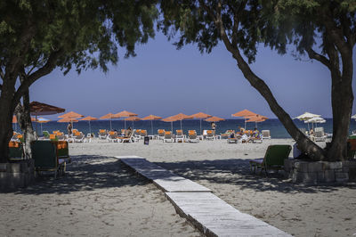 Floorboard by parasols and lounge chairs at beach against clear sky