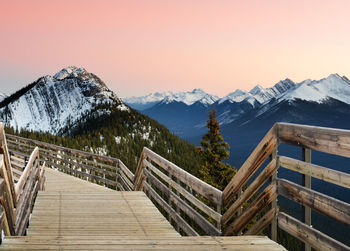 Wooden footbridge leading towards snowcapped mountains against clear sky