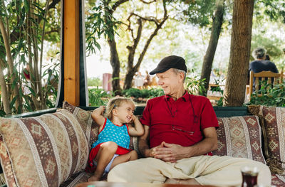 Grandfather with cute granddaughter sitting on seat in park