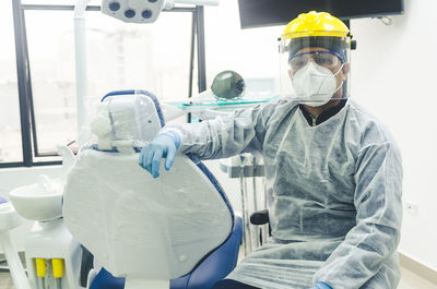 Portrait of dentist wearing mask and face shield sitting at clinic