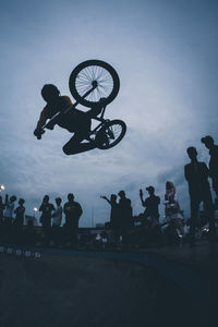 Low angle view of silhouette man performing stunt on bicycle at dusk