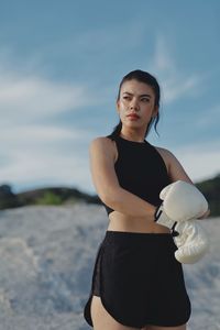 Portrait of young woman standing at beach against sky