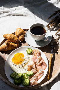 Breakfast in bed coffee cup, fried egg, bacon and croissants on wooden tray. 