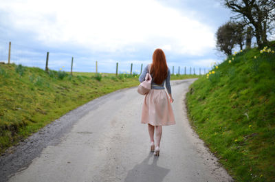 Rear view of young woman walking on country road