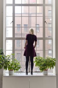 Rear view of woman standing on window sill