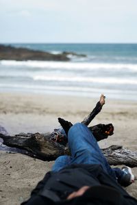 Low section of man lying down by bonfire at beach against sky